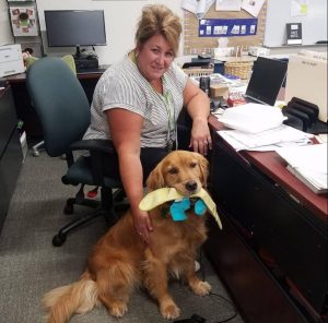 image: woman sitting at desk with dog sitting next to her